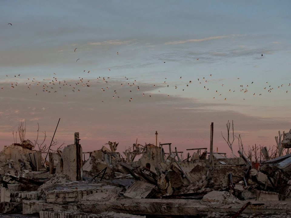 Gespenstische Trümmer vor einem bunten Himmel, an dem Vögel vorbeiziehen