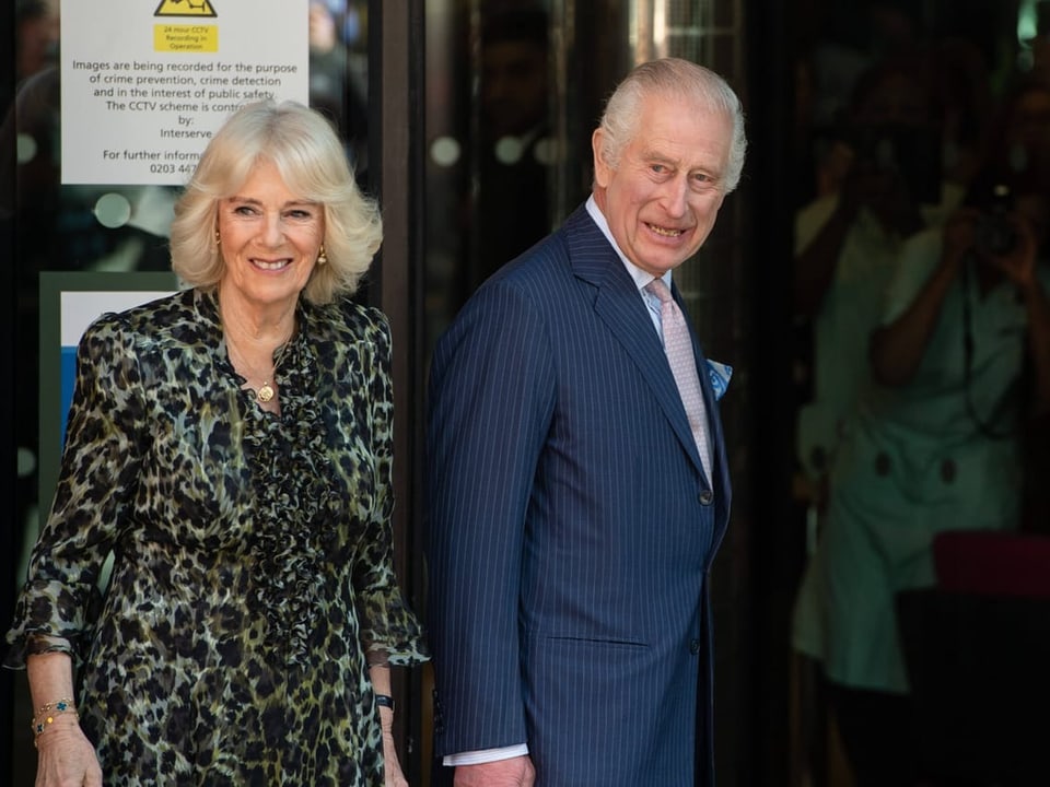 Charles und seine Frau stehen an einer Eingangstür und lächeln zurück. 