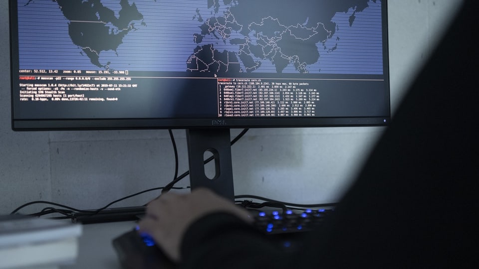 Person verwendet einen Computer mit Weltkarte und Datencodierung auf einem Monitor.