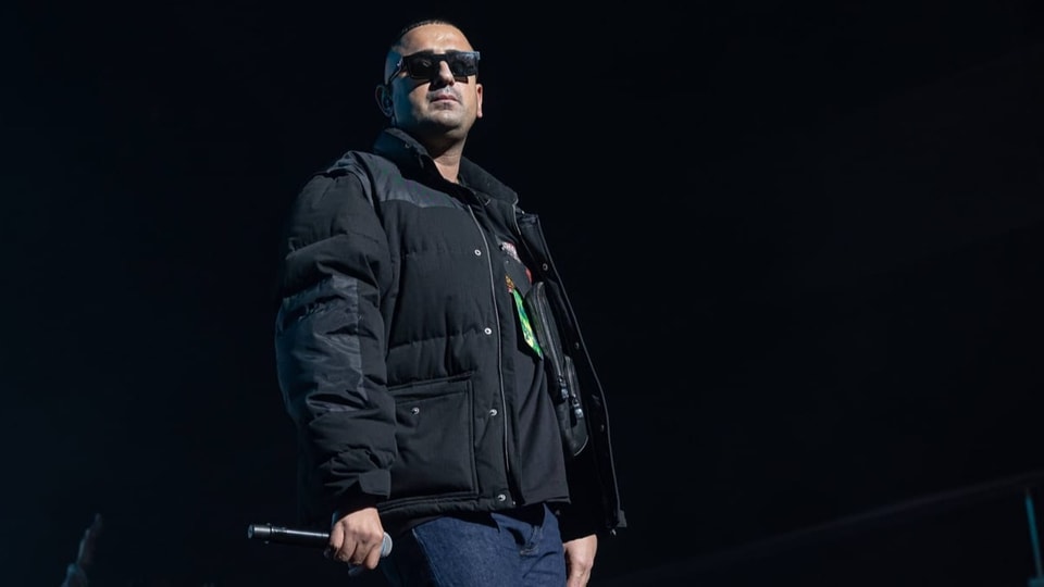 Der Rapper Haftbefehl mit Mikrofon in der Hand vor einem schwarzen Hintergrund.