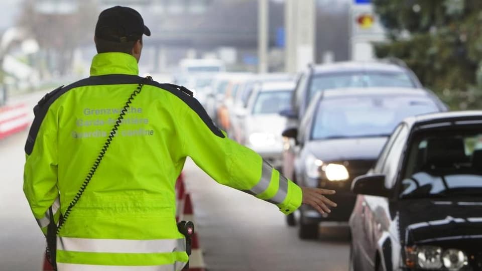 Ein Grenzwächter in einer gelben Jacke winkt eine Autokolonne durch