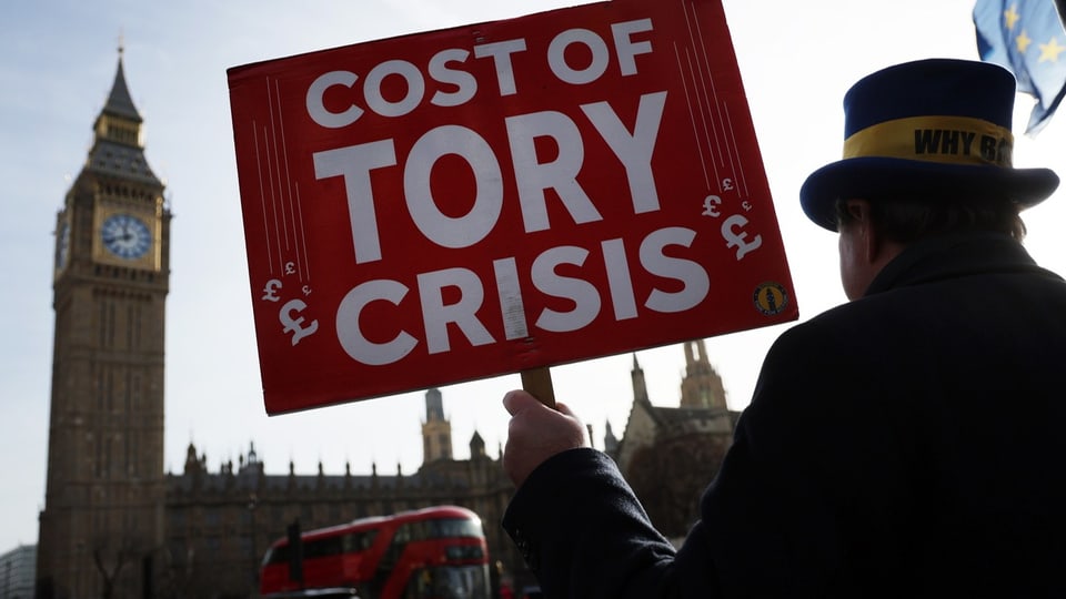 Ein Mann steht mit einem Plakat «Kosten der Tories-Krise» vor dem Parlamentsgebäude. 