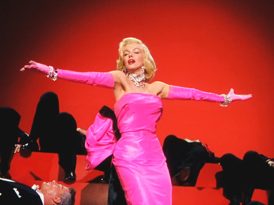Marilyn Monroe in pinkfarbenem Kleid vor rotem Hintergrund.