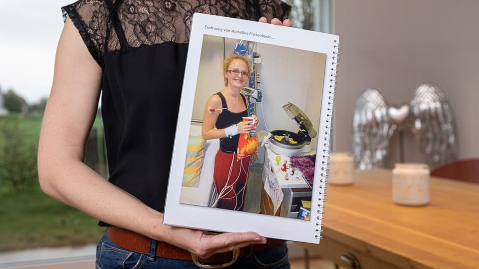 Eine Frau hält ein Fotoalbum mit einem Bild von einer Frittiermaschine im Spital.