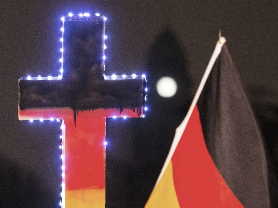 Ein Kreuz in den deutschen Nationalfarben und eine Landesfahne