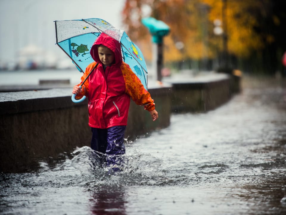  Ein Kind mit Schirm und wasserdichten Hosen watet durch das überflutet Ufer am Lago Maggiore.