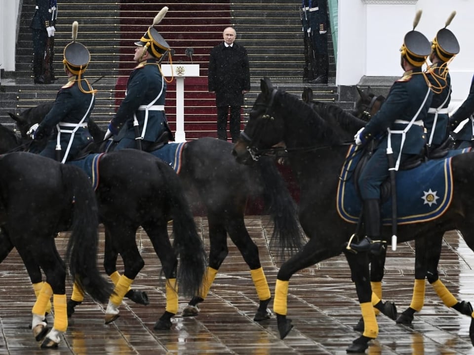Putin steht auf einer Treppe im Kreml. Vor ihm sitzt die Ehrengarde auf Pferden.