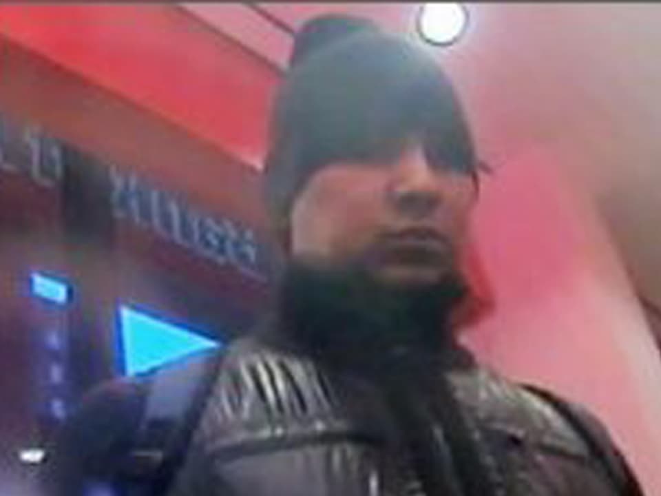 Ein Mann mit schwarzer Mütze, schwarzer Jacke und Rucksack schaut neben der Kamera vorbei.