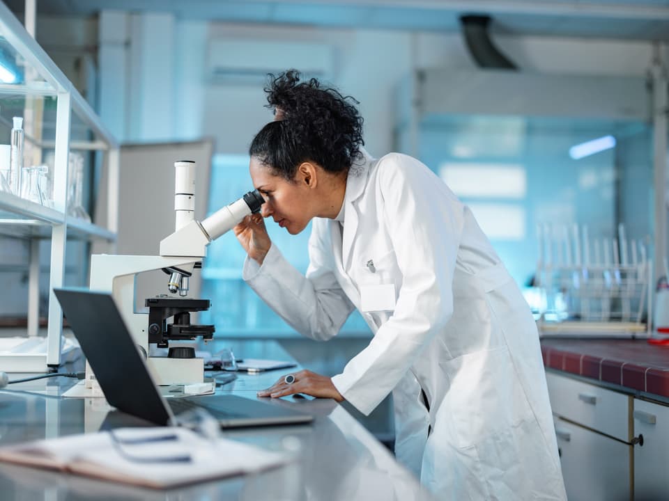 Wissenschaftlerin untersucht Proben durch ein Mikroskop im Labor