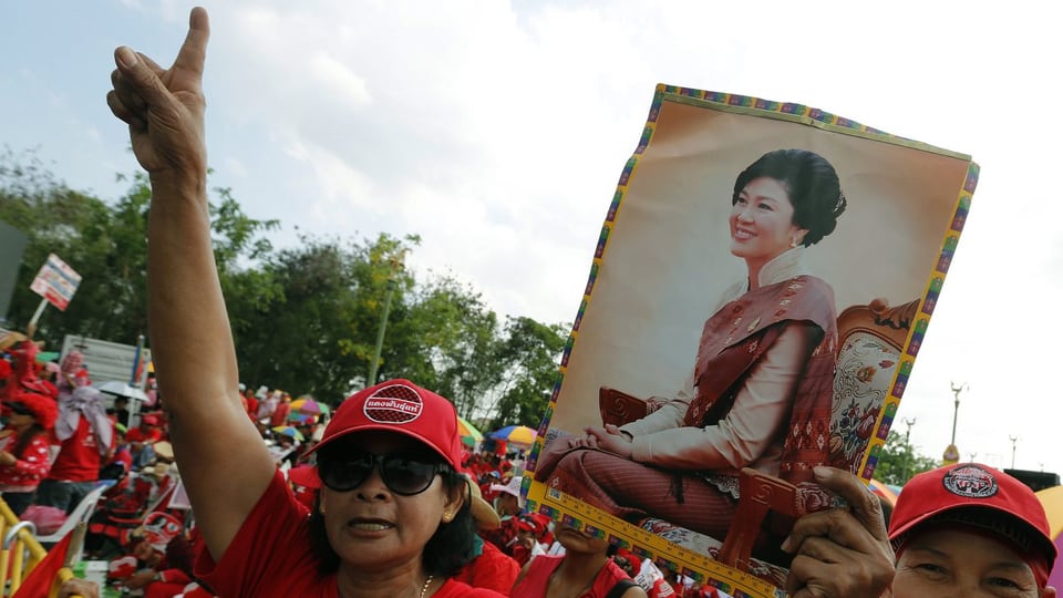 Thailänder – rot gekleidet – tragen Bilder in den Händen und schreien Parolen. 