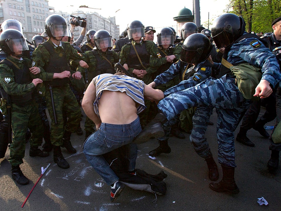 Polizisten, die mit Fusstritten einen Demonstranten malträtieren.