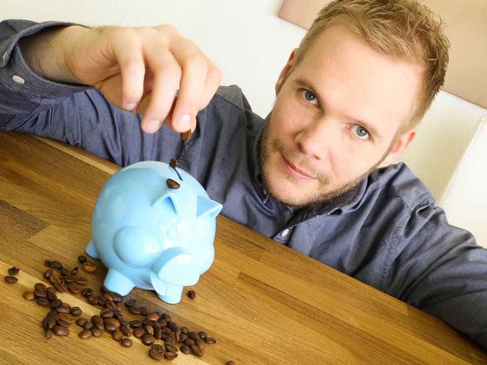 Stefan Siegenthaler lässt Kaffeebohnen aufs Sparschwein fallen.
