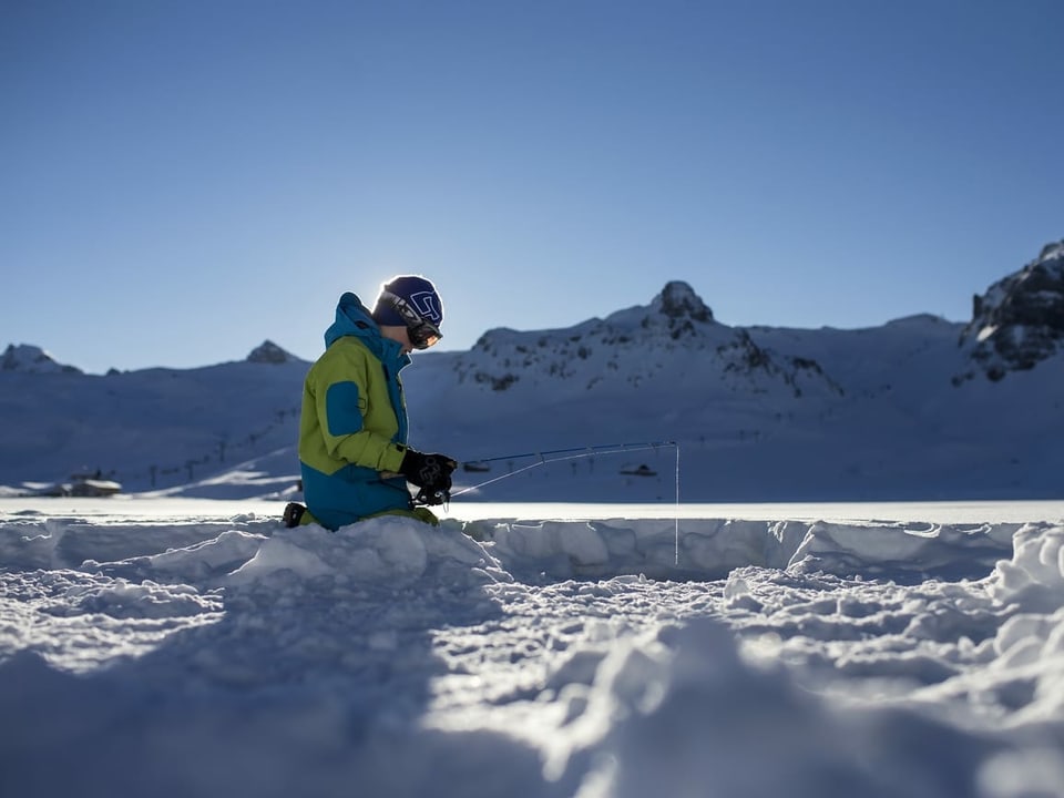 Ein Junge kniet auf einem gefrorenen See und hält eine Angel in ein Eisloch.