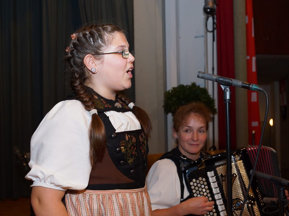 Die junge Jodlerin singt stehend und wird von einer erwachsenen Musikantin am Akkordeon begleitet.