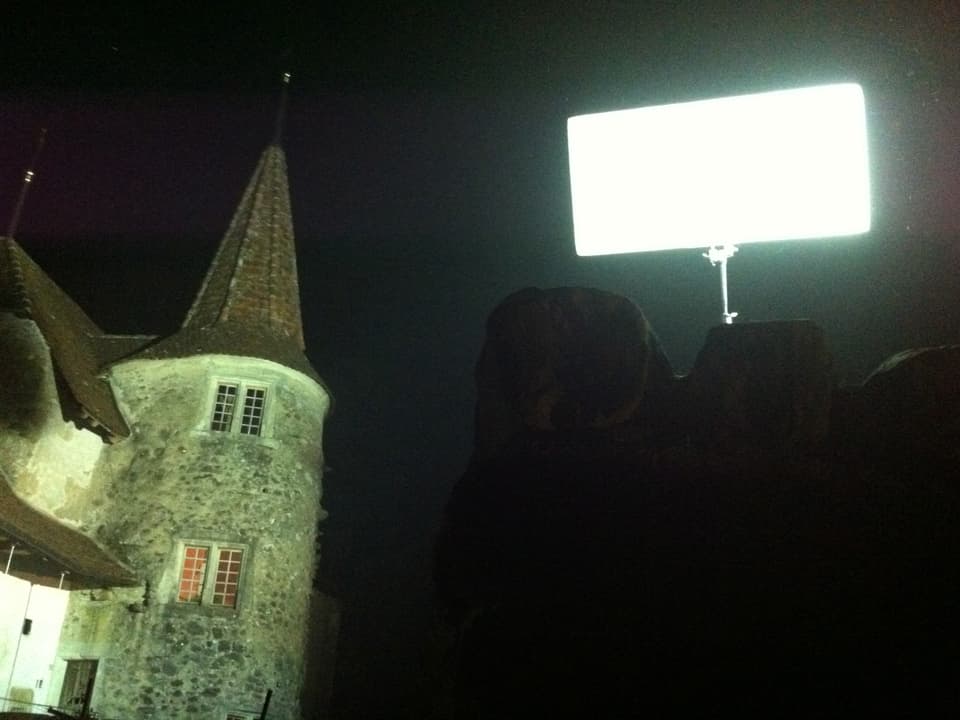Ein Scheinwerfer steht neben einem Schlossturm in der Nacht.