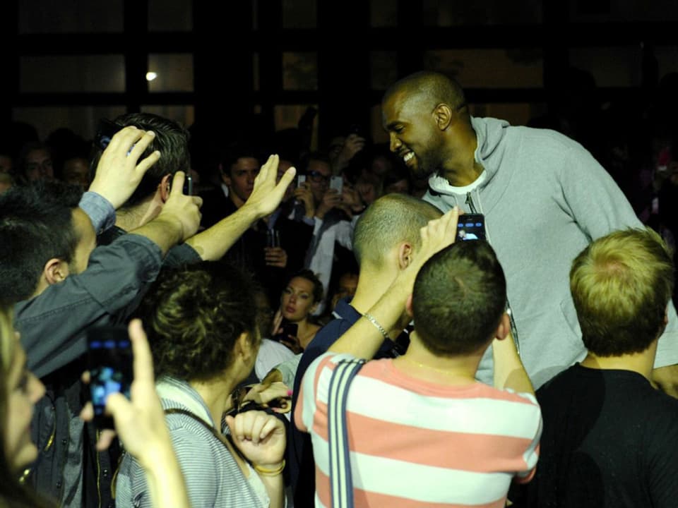 Fans des Rappers umringen Kanye West und fotografieren ihn mit ihren Smartphones.