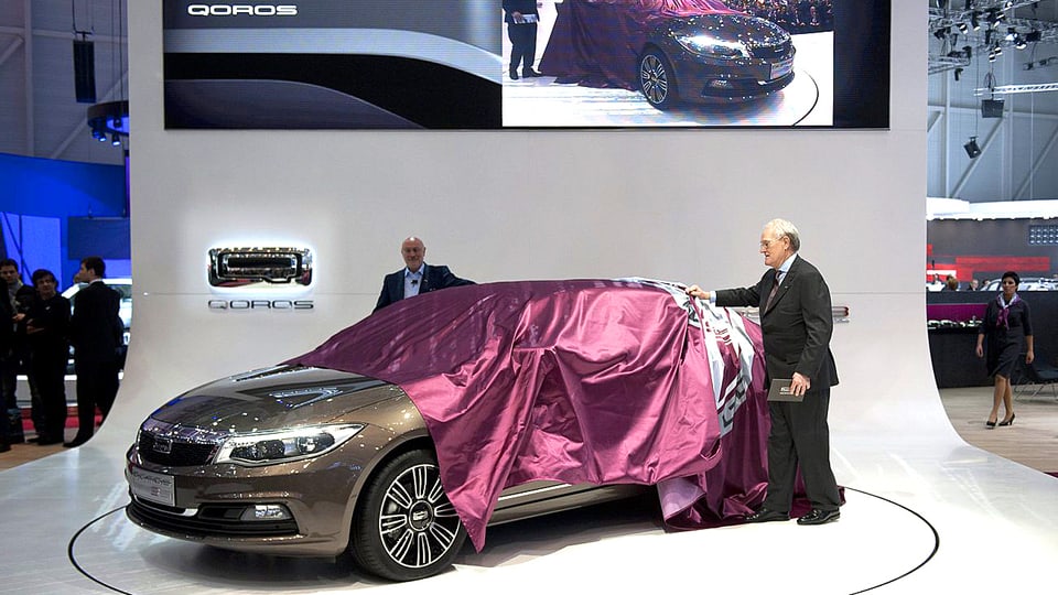 Zwei Präsentatoren ziehen die violette Sichtschutz-Plane von einem neuen Modell des Qoros anlässlich seiner erstmaligen Präsentation am Genfer Automobilsalon im Frühjahr 2013.