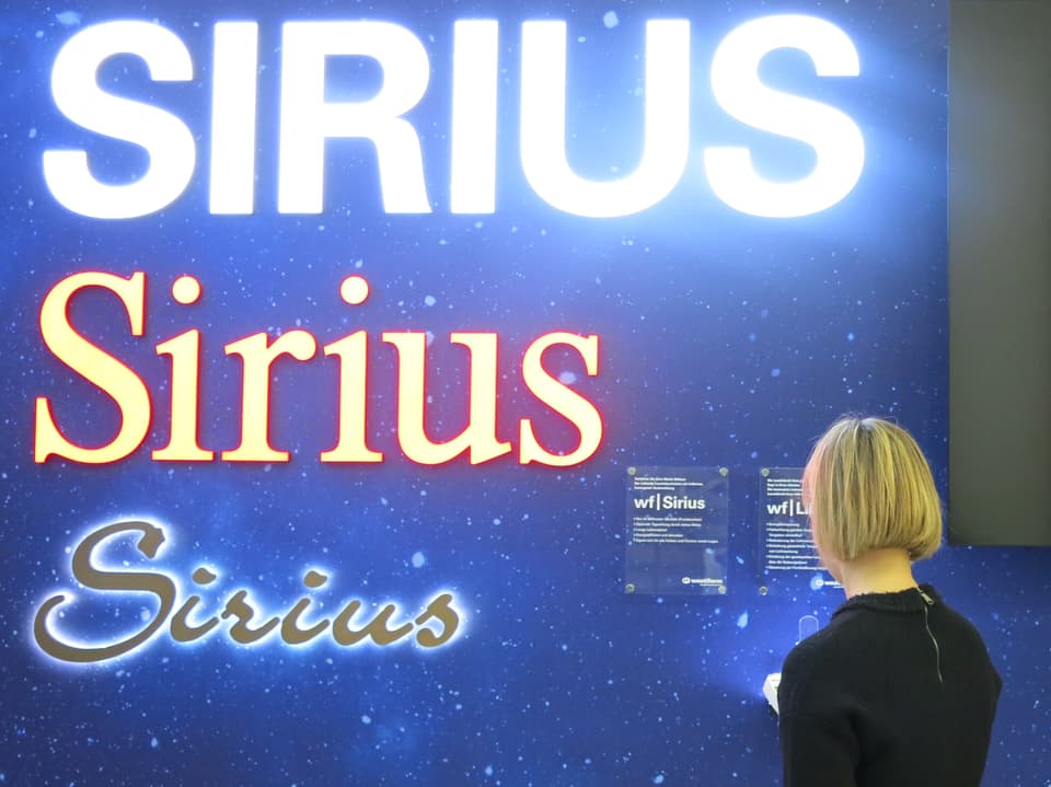 Anna Aebischer vor einer Wand mit Leuchtreklamen in der selber entwickelten Sirius-Schrift. 