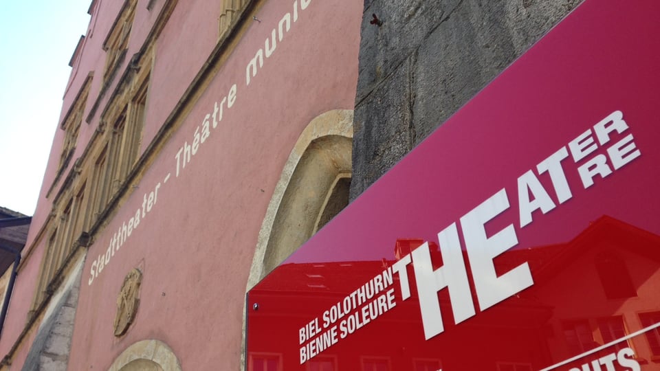 Theater Biel Solothurn von aussen betrachtet, im Vordergrund eine rote Tafel mit weisser Schrift.