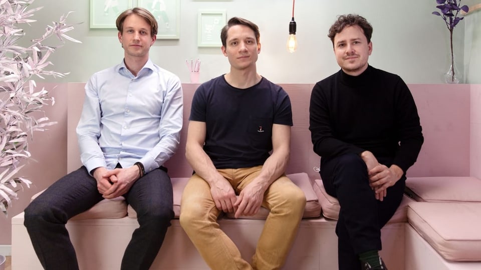 Die drei Gründer der Lernplattform «evulpo» sitzen auf einem rosafarbenen Sofa.  