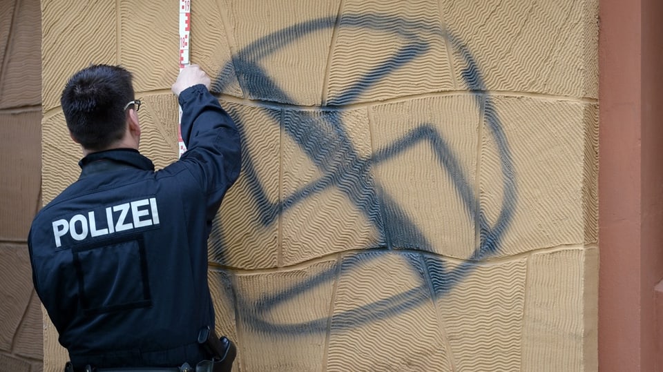Ein Polizist entfernt Schmiererien mit einem Swastika.