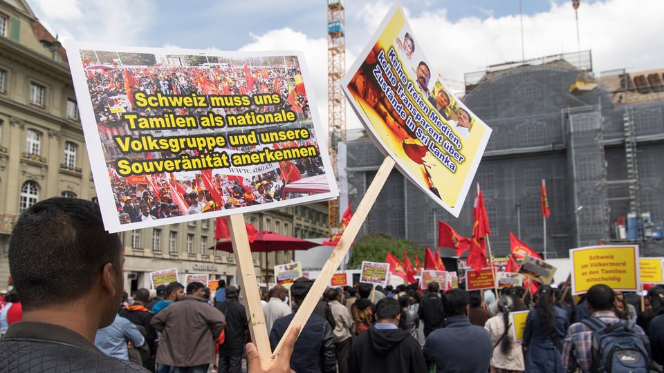 Rückenansicht von demonstrierenden Tamilen in Bern mit Protestschildern. 
