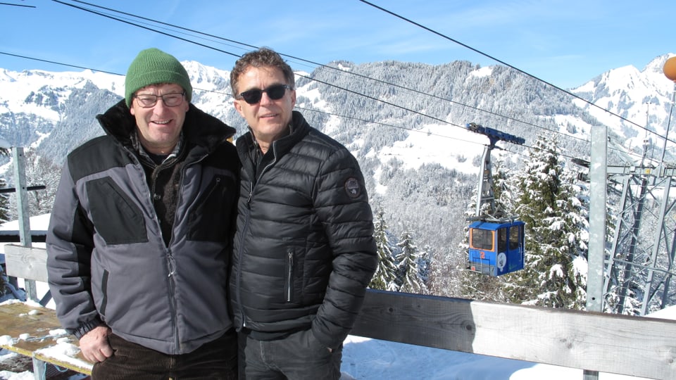 zwei Männer vor Seilbahn und Bergpanorama