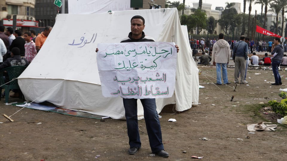 Ein Mann hält ein Plakat mit arabischer Schrift.
