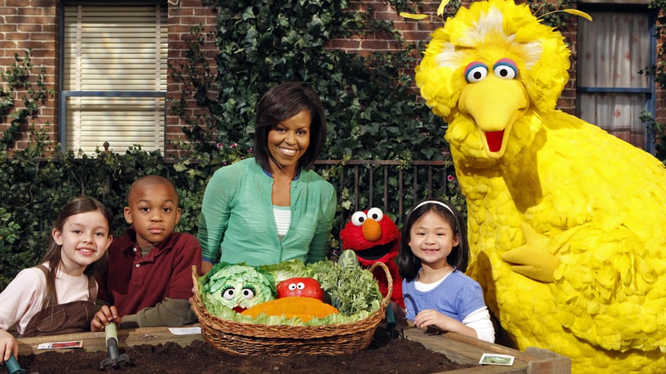 Michelle Obama in der Sesamstrasse, vor ihr un den Kindern ein Korb voller Gemüse.