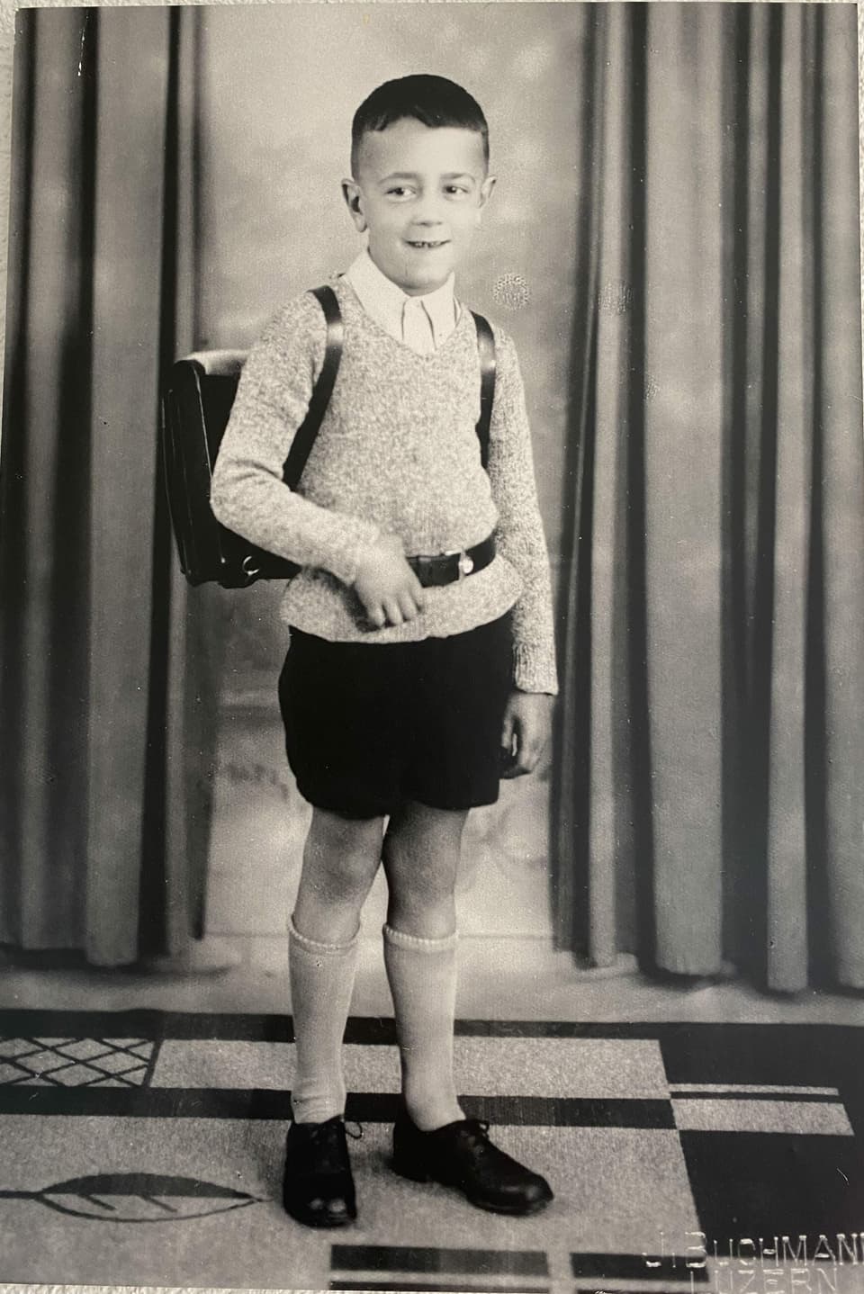 Ein Bub mit einem Schulsack auf einem Schwarzweiss-Foto.