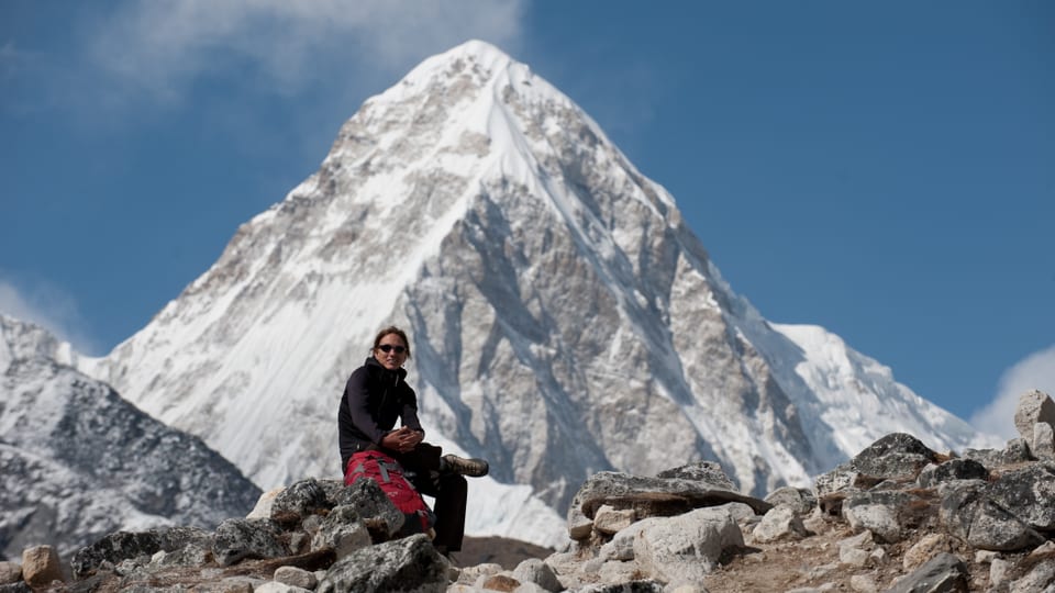 Frau sitzt auf einem Stein, im Hintergrund der Mount Everest.