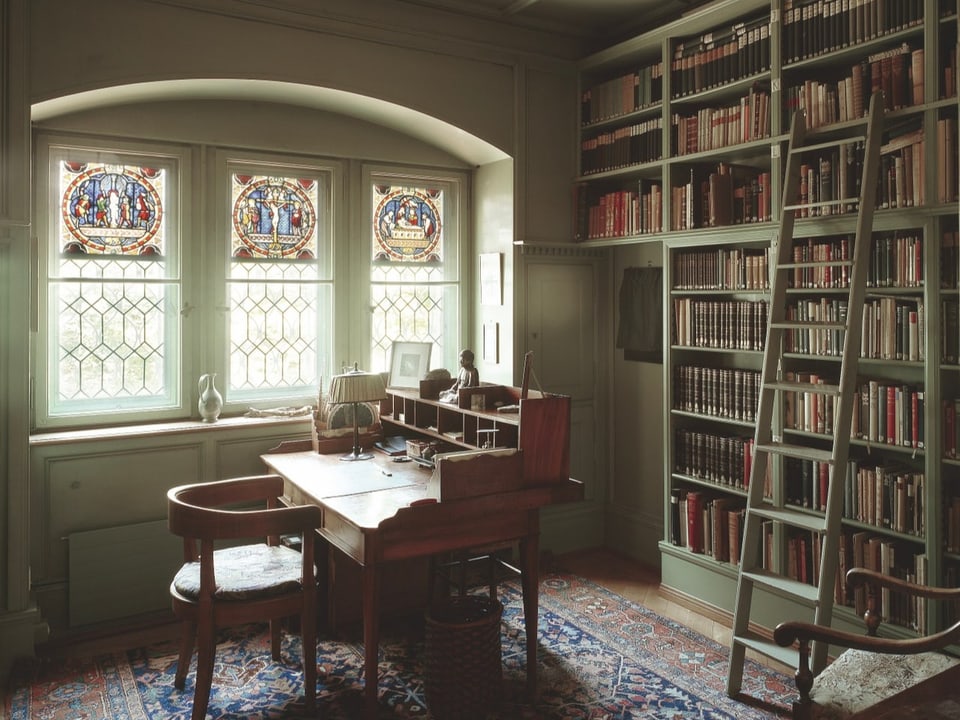 Im Inneren des C G. Jung-Hauses befindet sich ein weisses Regal mit alten Büchern, davor ein antiker Tisch.