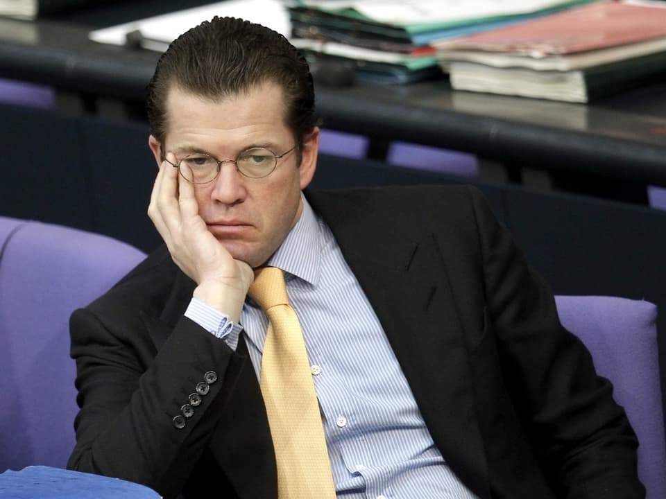 Guttenberg sitzt im Bundestag und stützt sein Gesicht mit seiner Hand.