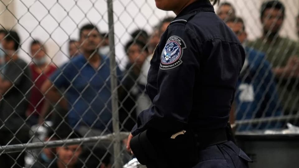 Polizistin vor einem Gitter, Migranten dahinter