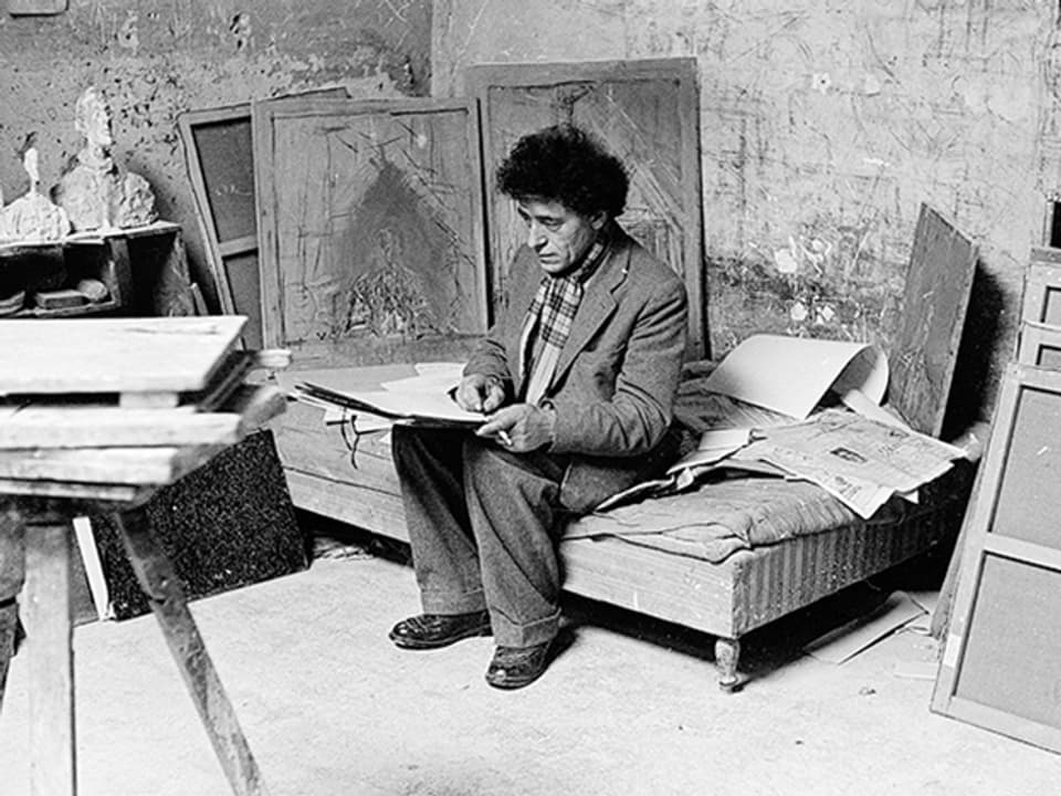 Alberto Giacometti sitzt zeichnend auf dem Bett.