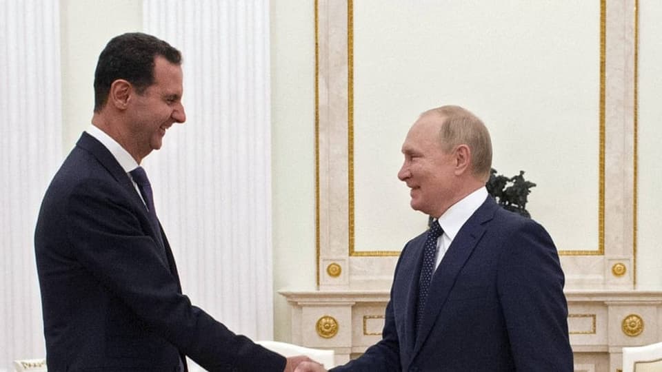 Bashar al-Assad mit Putin: Zwei Männer, die sich die Hand schütteln, Assad ist ein Kopf grösser als Putin.
