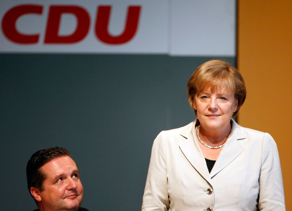 Mappus sitzend schaut auf die stehende Angela Merkel.