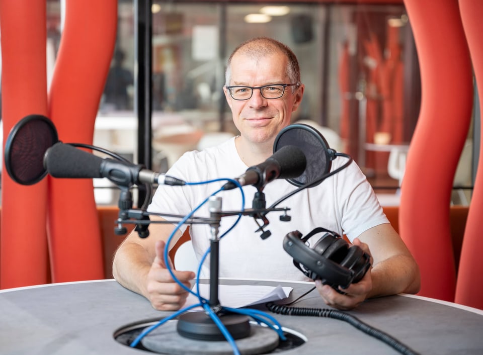 Markus Gasser sitzt in einem Sendestudio vor einem Mikrophon.