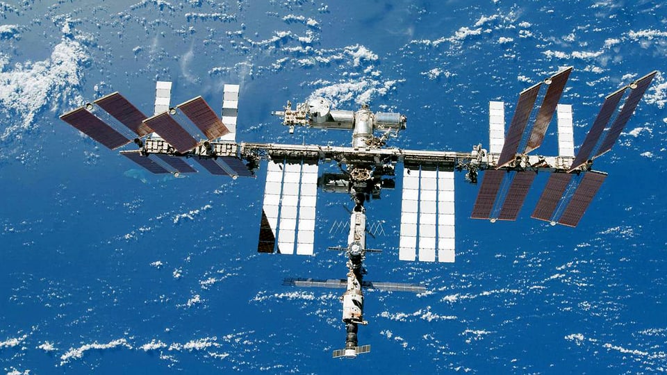 Blick auf die Raumstation ISS. Im Hintergrund das helle Blau der Erdkugel mit kleinen Wölklein.