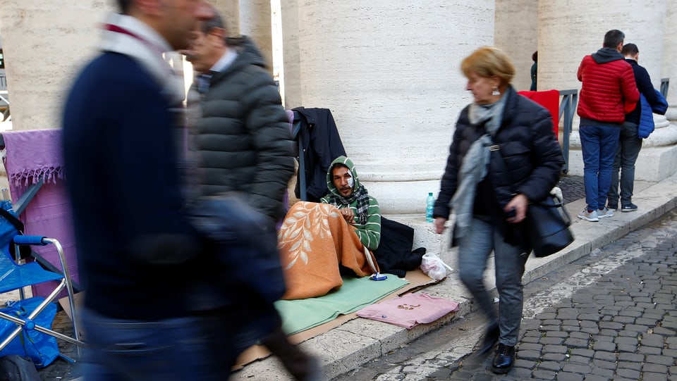 Menschen gehen an Obdachlosen auf dem Petersplatz vorbei