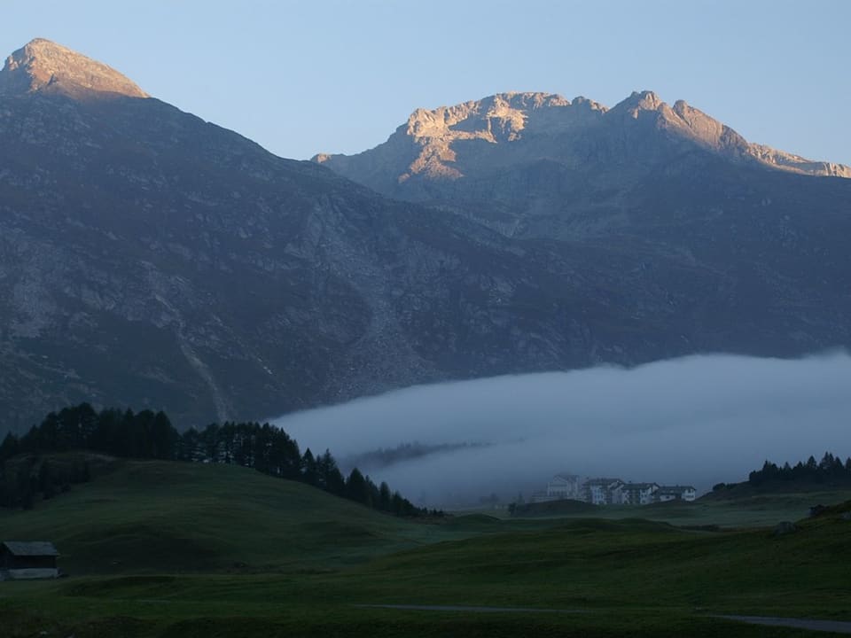 Blick über das Oberengadin. Im Hintergrund zwei Berge, in der Mitte über dem Tal ein wurstförmiges Wolkengebilde. 