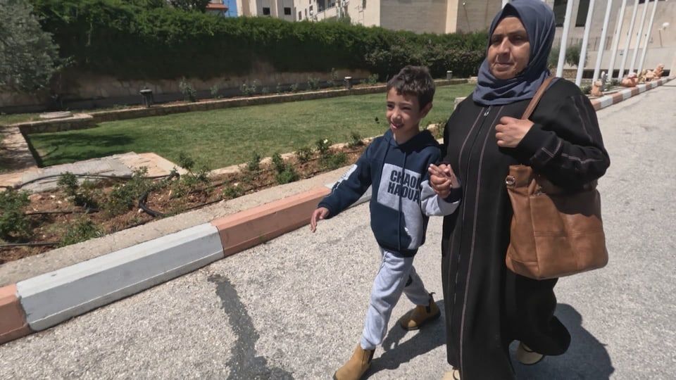 Awatef hält die Hand von ihrem Sohn Naeem. Sie laufen gemeinsam auf einem Gehweg zum Spital. 