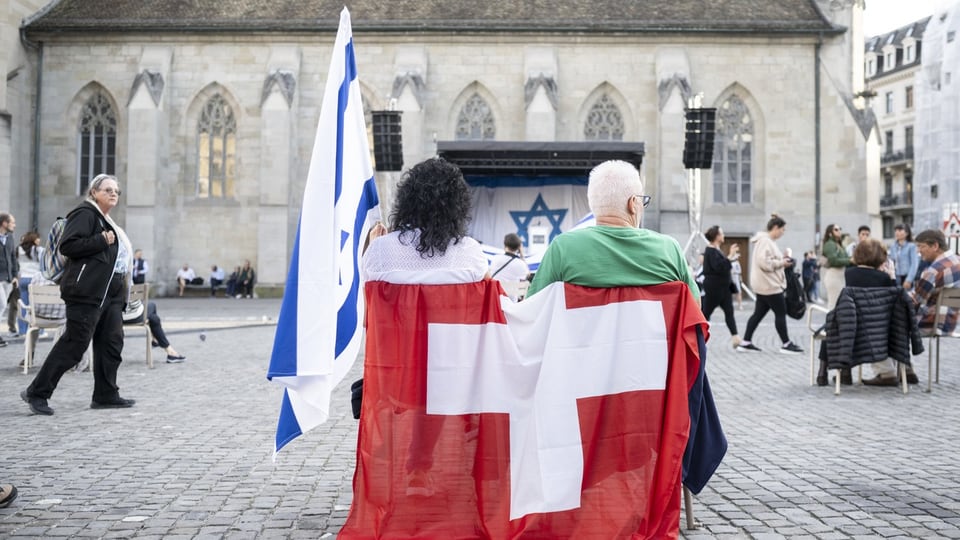 Ein Paar sitzt auf dem Münsterhof:  um ihren Stuhl gehängt ist eine Schweizer Flagge; daneben steht eine Israelische.