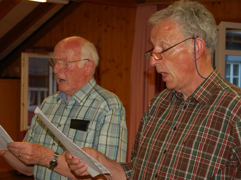 Zwei ältere Männer mit Notenblatt beim Singen.