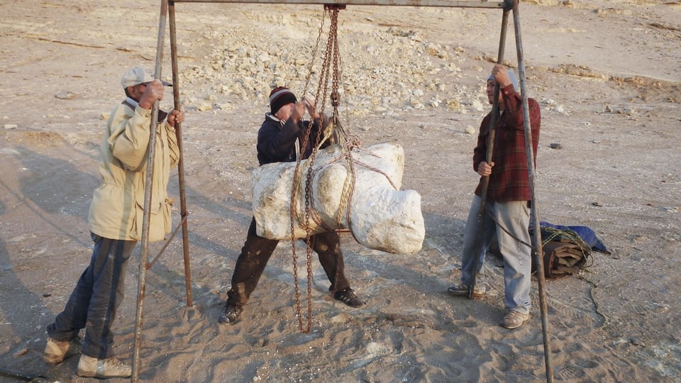 Drei Männer mit einem grossen Knochen der an Seilen hängt