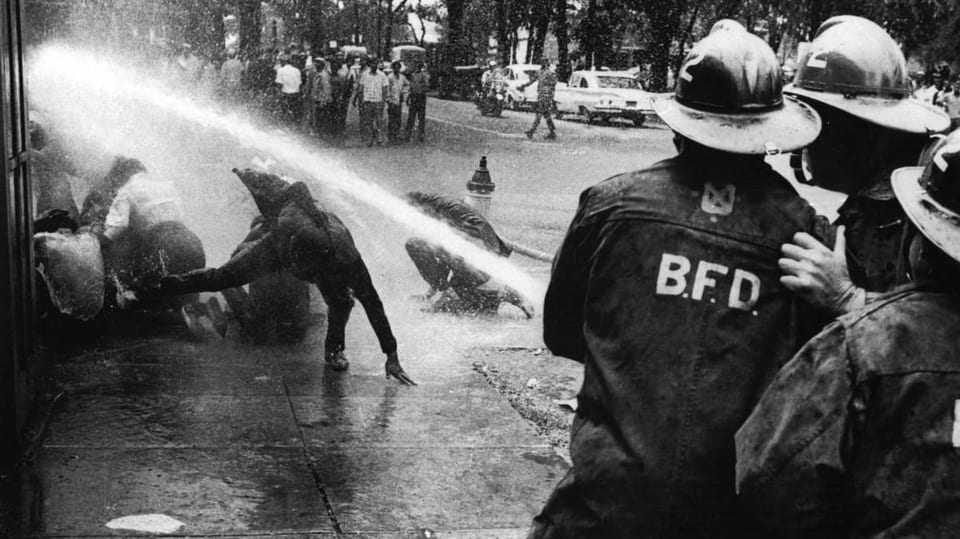 Feuerwehrleute richten den Wasserschlauch auf Demonstrierende.