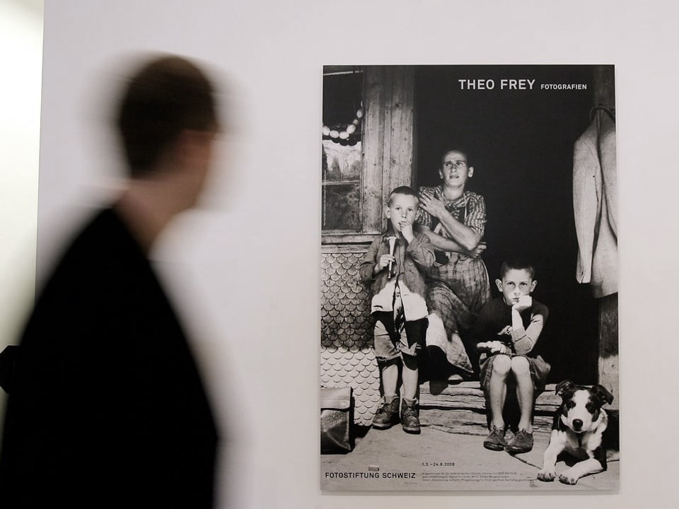 Ein Mann in einer Ausstellung geht an einem Foto vorbei, das eine Frau mit zwei Kindern zeigt.