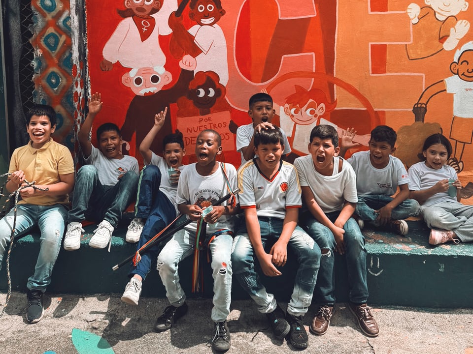 Mehrere Jungs sitzen aufgereiht und fröhlich vor einer Wand mit einem farbigen Graffiti