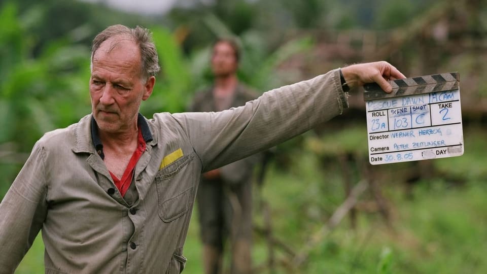 Mann hält Filmklappe in einer Dschungel-Landschaft.