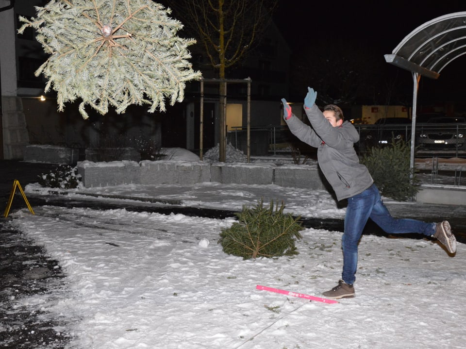 Mann wirft Christbaum. Schnee am Boden.